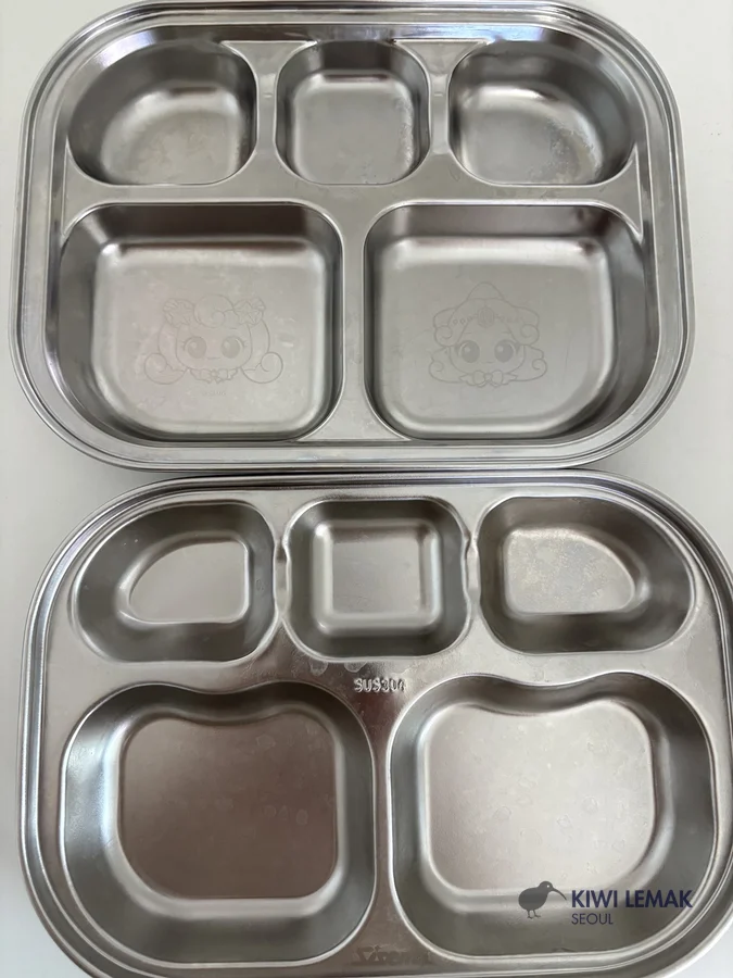 A real stainless-steel divided lunch tray used at a Korean daycare, with cute character engravings in two of the compartments