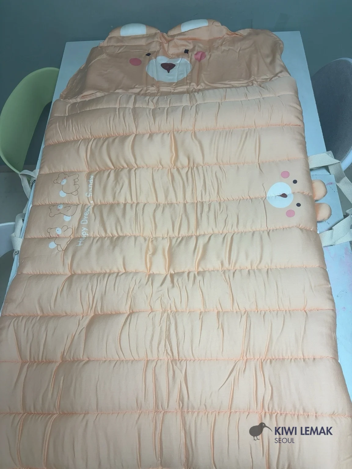 A Korean daycare nap bedding set fully unfolded across two joined desks to show its actual length, with a bear-shaped hood at one end