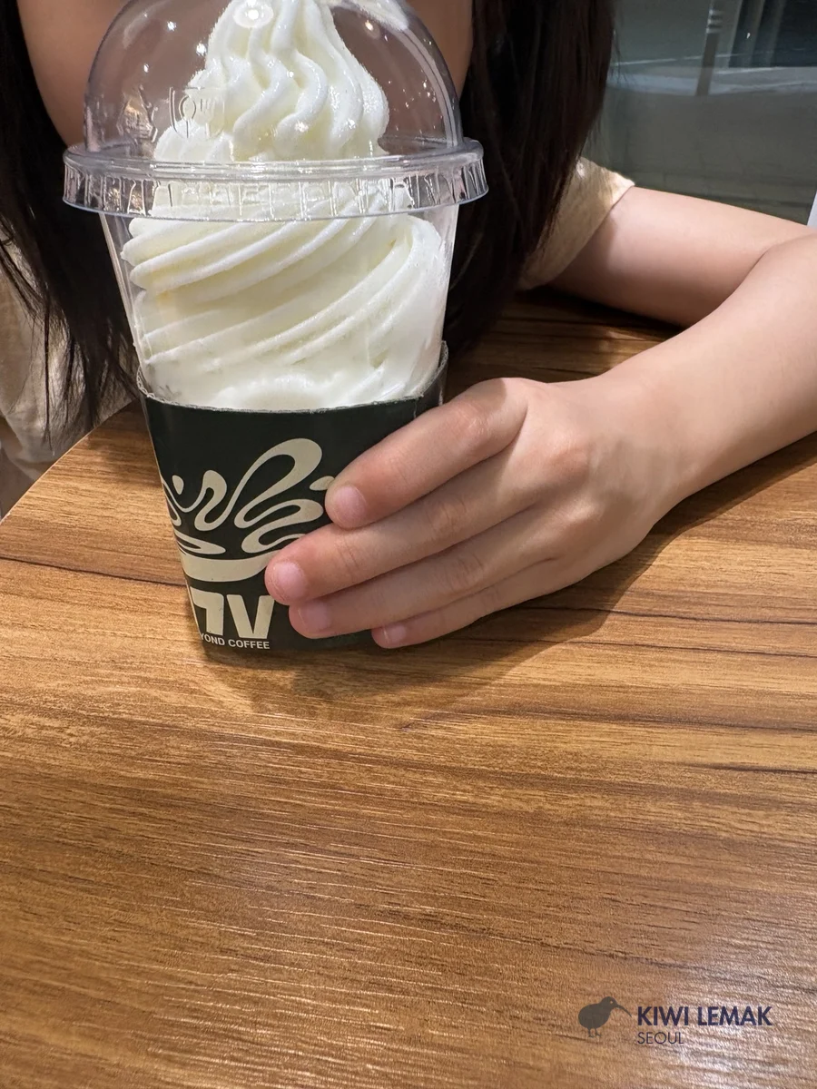 A hand holding a soft-serve ice cream cup with a coffee shop logo on the sleeve