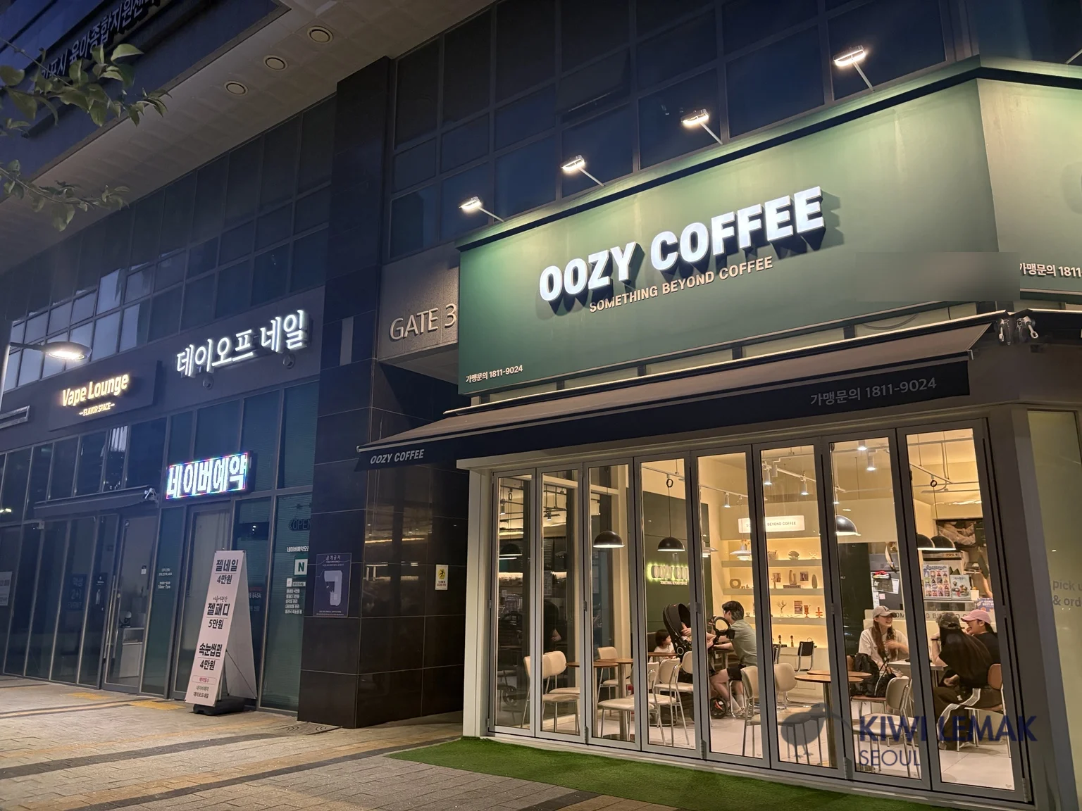 Evening exterior of a Korean coffee shop with a lit green storefront sign reading OOZY COFFEE