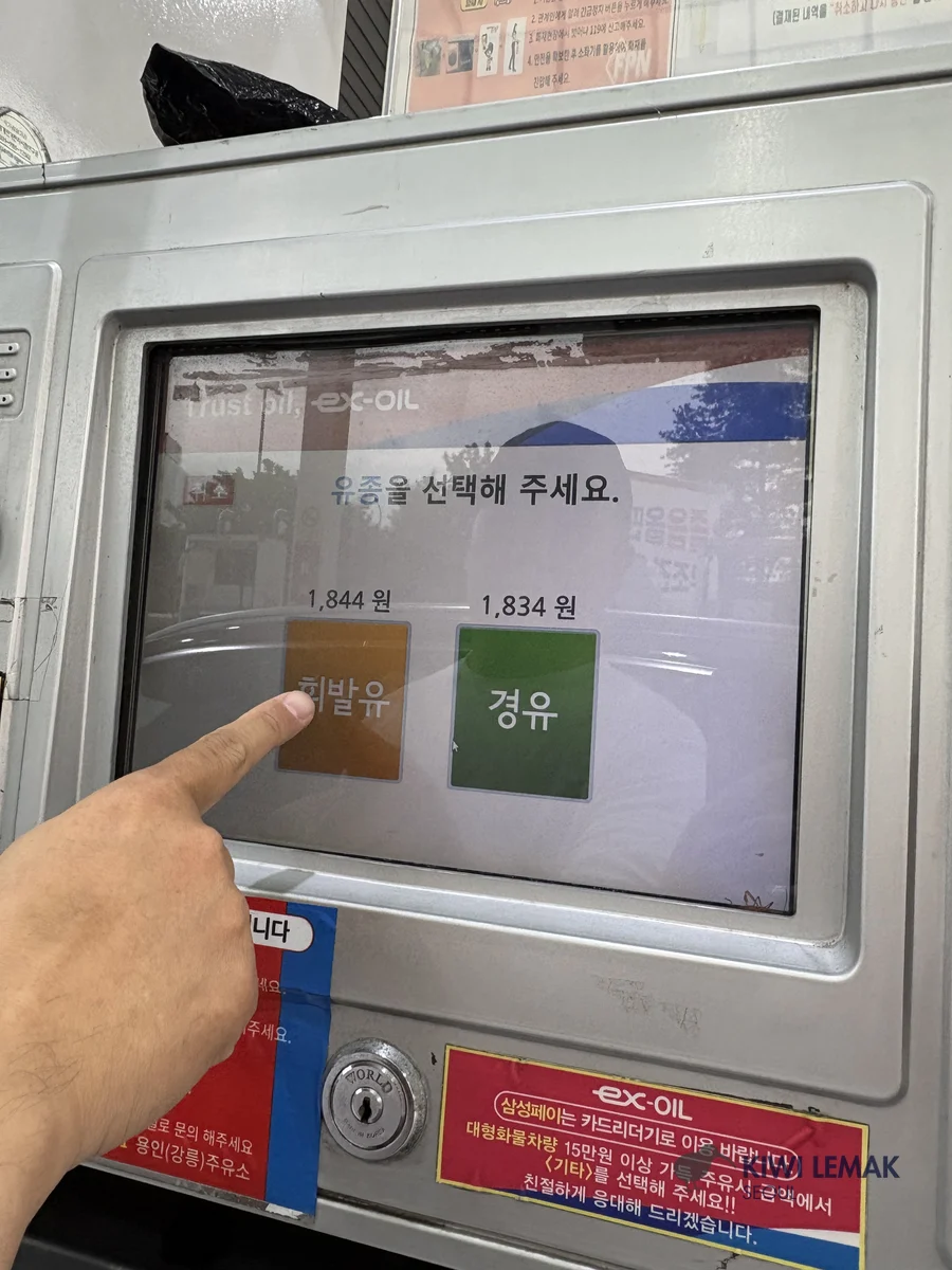 A finger touches a gas pump touchscreen displaying two fuel options with their prices: gasoline at 1,844 won and diesel at 1,834 won per liter.